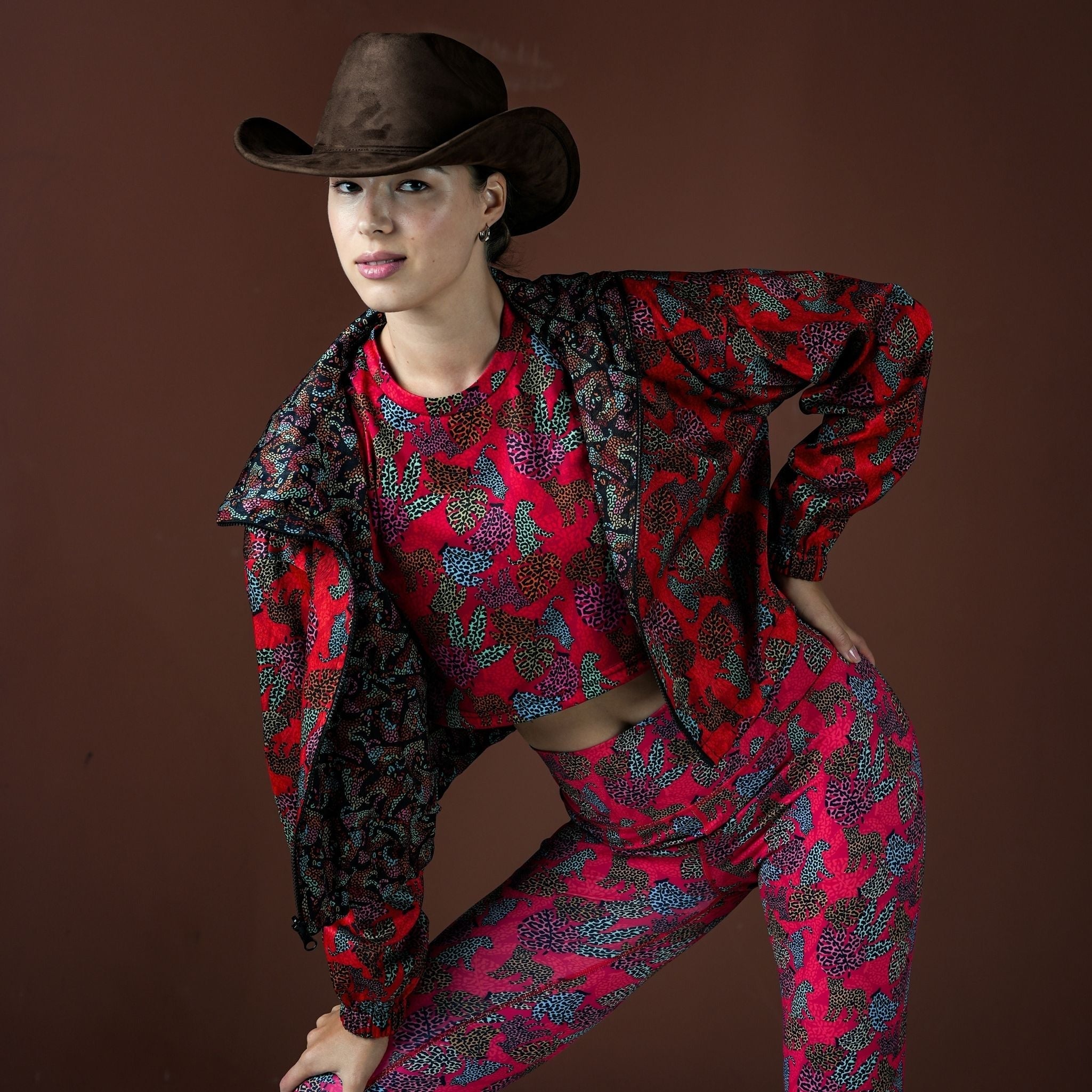 Person wearing a red and black patterned outfit with a cowboy hat on a brown background