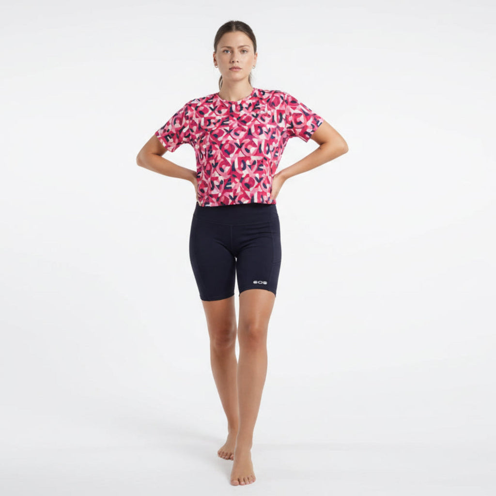 Woman wearing a pink patterned shirt and black shorts on a white background
