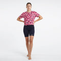 Woman wearing a pink patterned shirt and black shorts on a white background